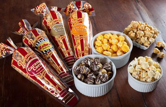 mini cones of assorted gourmet popcorn next to snack bowls on wood table