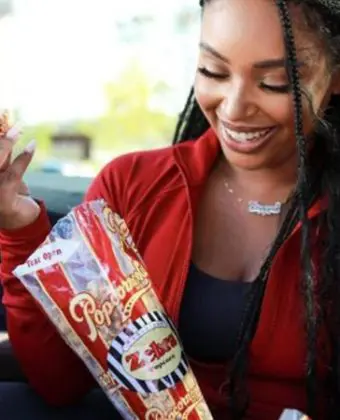 A picture of a woman snacking on gourmet popcorn flavored Zebra® Popcorn in a car.