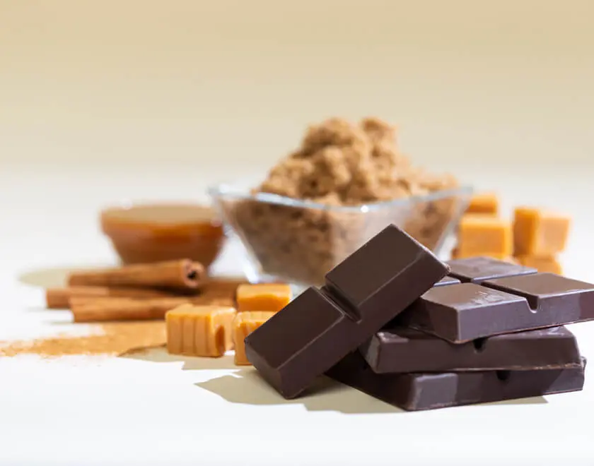 A picture of dark chocolate, caramel, cinnamon sticks and a bowl brown sugar.