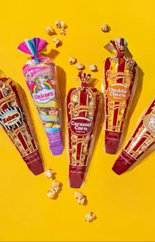 Picture of five gourmet mini cones flavored of Zebra® Caramel Corn, Cheddar Cheese, Kettle Corn and Unicorn. With yellow background and popcorn kernels.